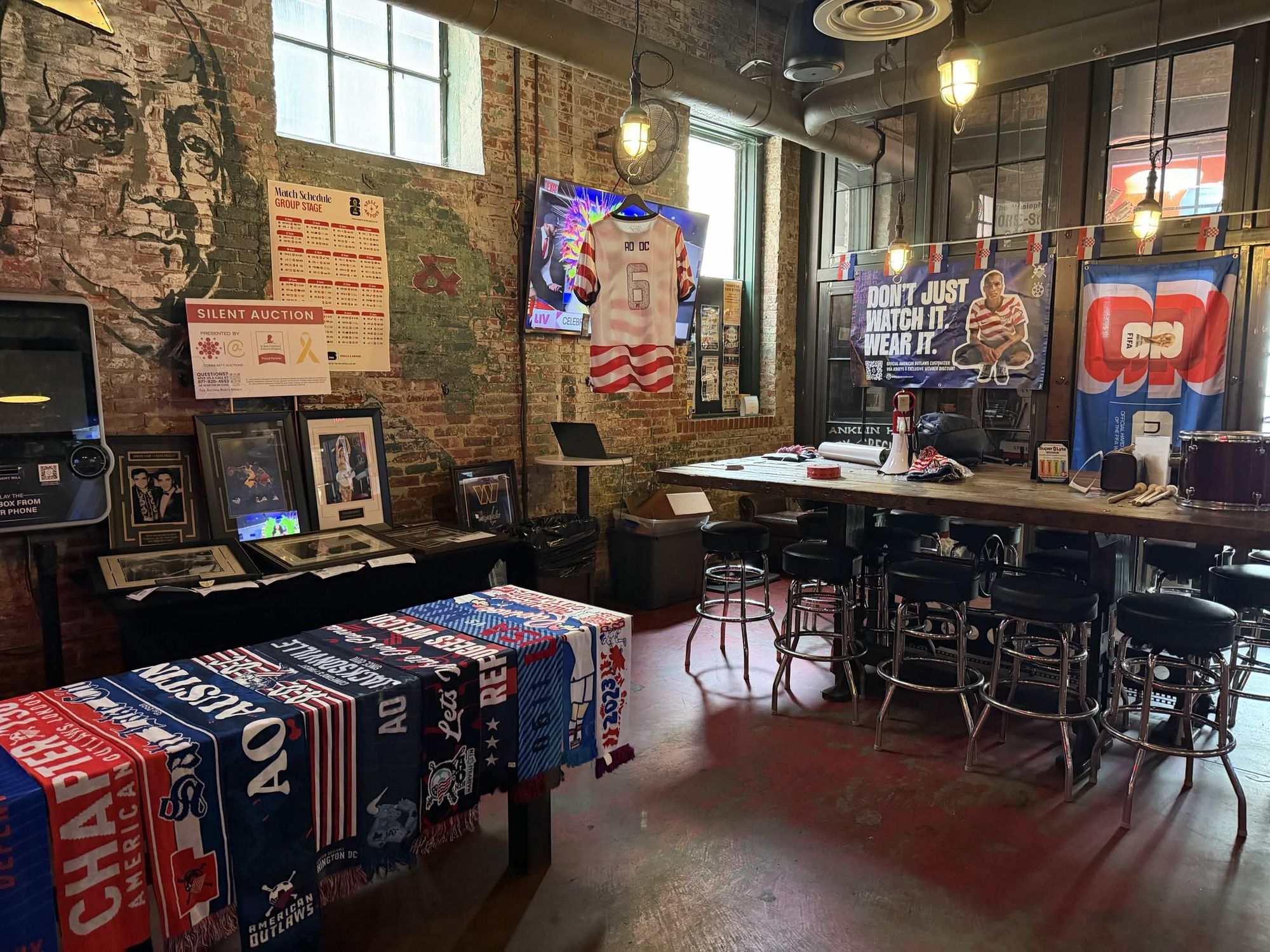 An American Outlaws chapter bar set up for a FIFA World Cup™ watch party, with the WorldSoccerShop banner hung and chapter scarves laid out
