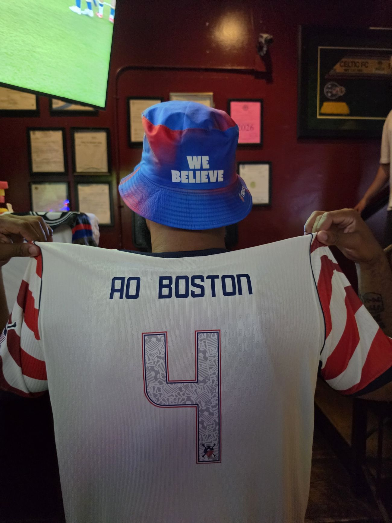 A chapter member holding up a customized American Outlaws Boston USA jersey inside the watch-party bar