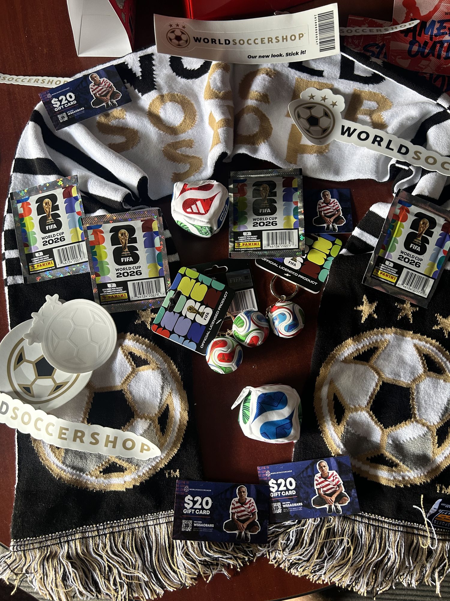 The WorldSoccerShop chapter kit laid out: scarves, stickers, gift cards, Panini FIFA World Cup™ sticker packs, keychains, and a soccer-ball tap handle